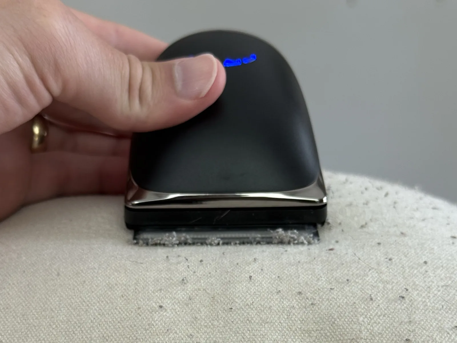 The Couch Shaver head-on, charge lights lit, mid-pass across a pilled cushion.